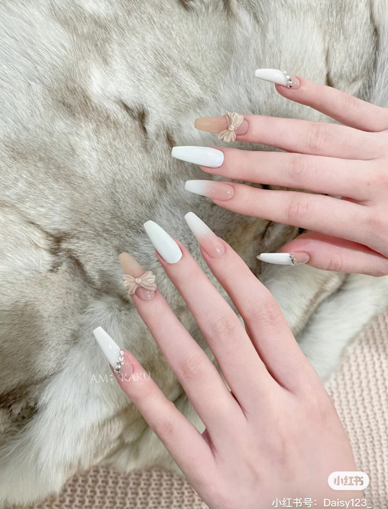 Bàn tay với móng tay được trang trí nghệ thuật, có nơ và đá, trên nền lông mềm mại.