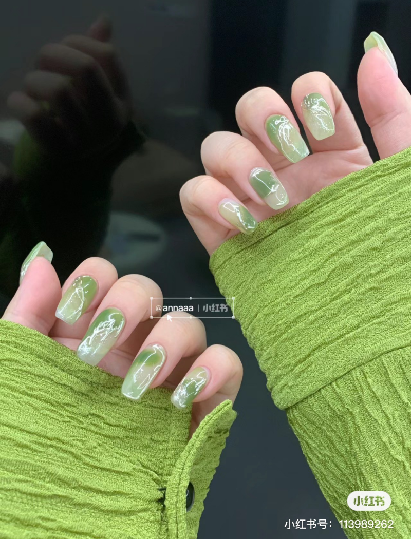 Bàn tay với móng tay sơn màu xanh lá cây nhạt, thiết kế hoa văn, áo dài tay màu xanh.