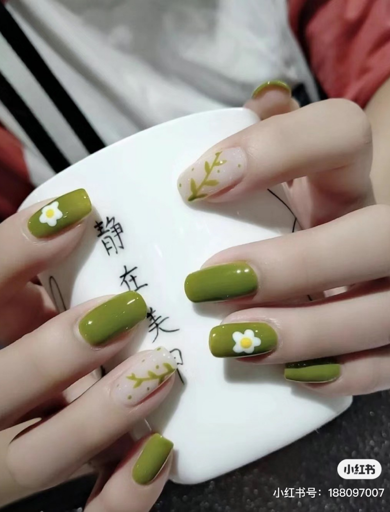Bàn tay với móng tay sơn màu xanh và họa tiết hoa cỏ, cầm một chiếc cốc trắng có chữ.