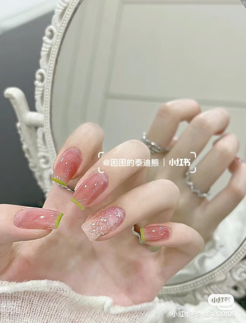 Bàn tay với móng tay sơn màu hồng nhạt, viền xanh lá, cầm gương trang trí hoa văn tinh xảo.