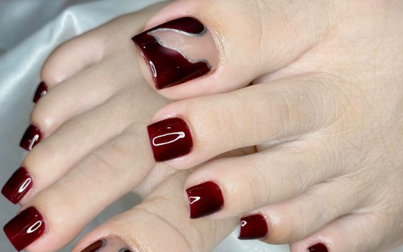 Bàn tay và chân với móng tay sơn màu đỏ đậm, móng tay cái có thiết kế độc đáo.