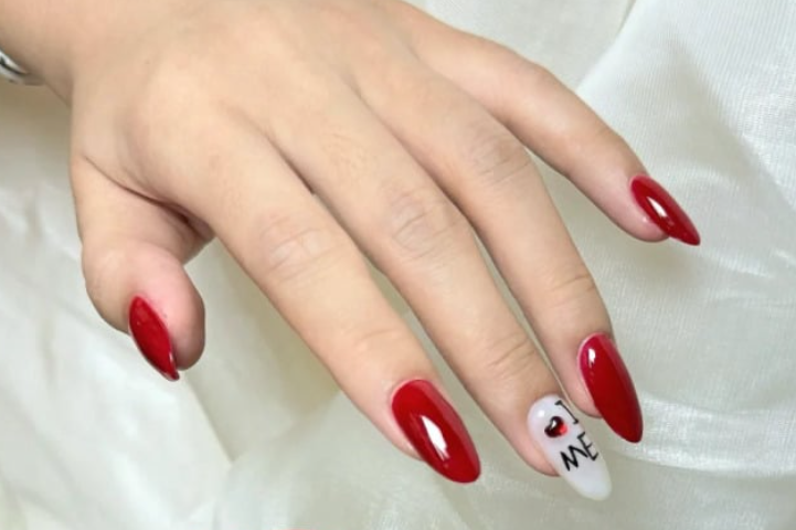 TOP 20+ Mẫu Nail Đỏ Trắng Đẹp Mê Mẩn Cho Nàng Thêm Xinh 5 Bàn tay với móng tay đỏ, một móng trắng có chữ và biểu tượng trái tim, đặt trên nền vải trắng.