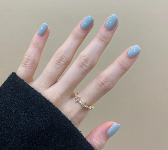 Tổng Hợp Mẫu Nail Màu Xanh Dương Nhạt Đẹp Nhẹ Nhàng Hot Nhất 2025 3 Một bàn tay đeo nhẫn vàng có đính đá, móng tay sơn màu xanh nhạt, áo tay dài màu đen.