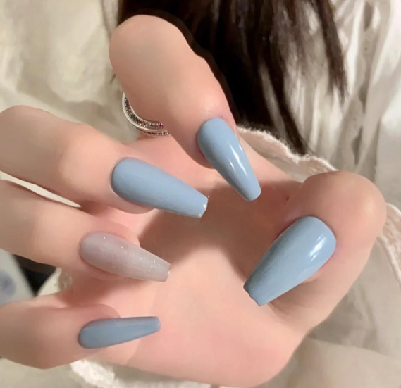 Tổng Hợp Mẫu Nail Màu Xanh Dương Nhạt Đẹp Nhẹ Nhàng Hot Nhất 2025 4 Bàn tay với móng tay dài sơn màu xanh nhạt, một móng màu trong suốt có ánh kim tuyến.