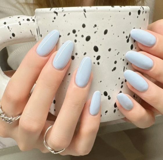 Tổng Hợp Mẫu Nail Màu Xanh Dương Nhạt Đẹp Nhẹ Nhàng Hot Nhất 2025 6 Bàn tay với móng tay sơn màu xanh nhạt cầm một chiếc cốc màu trắng có họa tiết đốm đen.