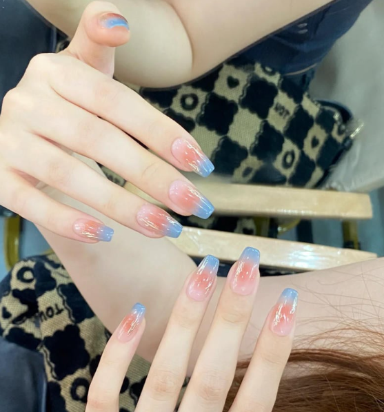 Tổng Hợp Mẫu Nail Màu Xanh Dương Nhạt Đẹp Nhẹ Nhàng Hot Nhất 2025 9 Bàn tay với móng tay sơn ombre màu xanh và hồng, nền là hoa văn hình học trên túi xách.