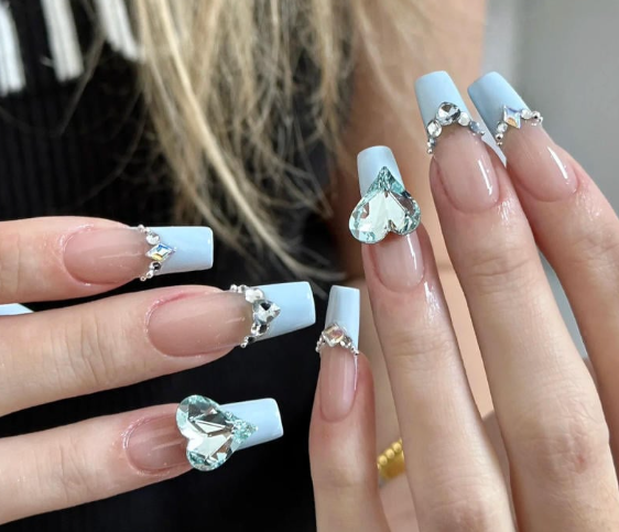 Tổng Hợp Mẫu Nail Màu Xanh Dương Nhạt Đẹp Nhẹ Nhàng Hot Nhất 2025 11 Bàn tay với móng tay dài, trang trí màu xanh nhạt và đính đá hình trái tim lấp lánh.