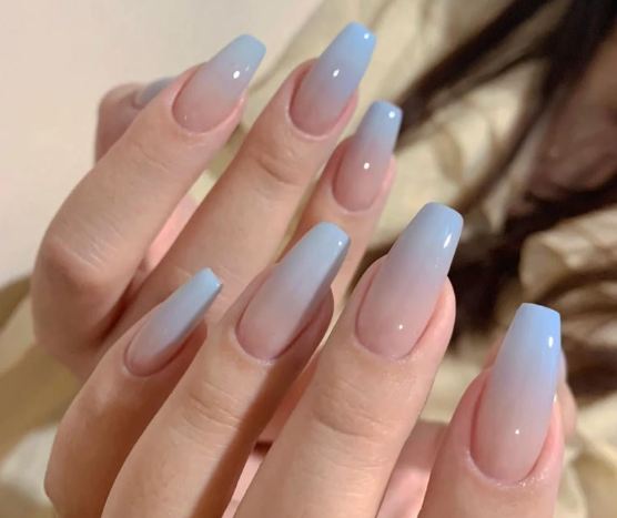 Tổng Hợp Mẫu Nail Màu Xanh Dương Nhạt Đẹp Nhẹ Nhàng Hot Nhất 2025 12 Bàn tay với móng tay dài, sơn ombre từ hồng nhạt đến xanh dương, nền mờ.
