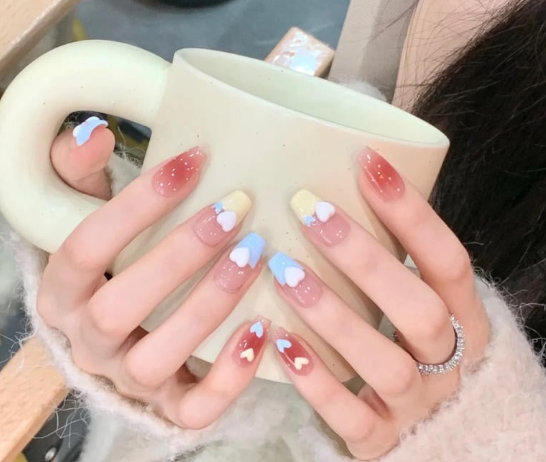 Tổng Hợp Mẫu Nail Màu Xanh Dương Nhạt Đẹp Nhẹ Nhàng Hot Nhất 2025 13 Tay cầm cốc màu nhạt, móng tay sơn hoạ tiết trái tim màu xanh, vàng, đỏ và trắng, đeo nhẫn bạc.