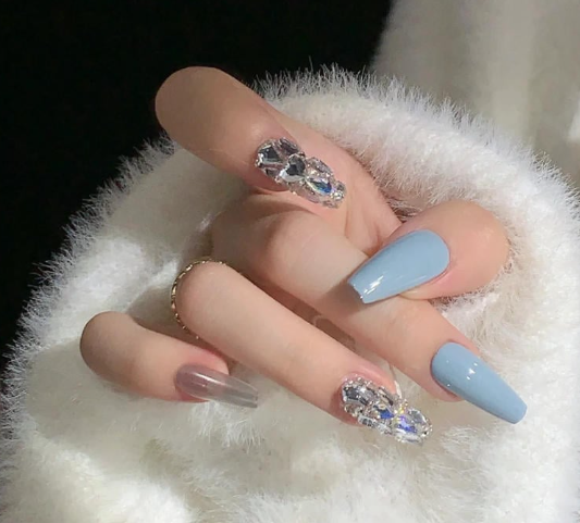 Tổng Hợp Mẫu Nail Màu Xanh Dương Nhạt Đẹp Nhẹ Nhàng Hot Nhất 2025 18 Bàn tay với móng tay trang trí màu xanh và đính đá, được đặt trên vải lông màu trắng.
