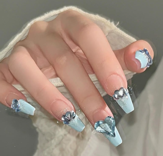 Tổng Hợp Mẫu Nail Màu Xanh Dương Nhạt Đẹp Nhẹ Nhàng Hot Nhất 2025 21 Bàn tay với móng tay dài, sơn màu xanh nhạt, trang trí bằng đá quý hình trái tim và hoa lấp lánh.