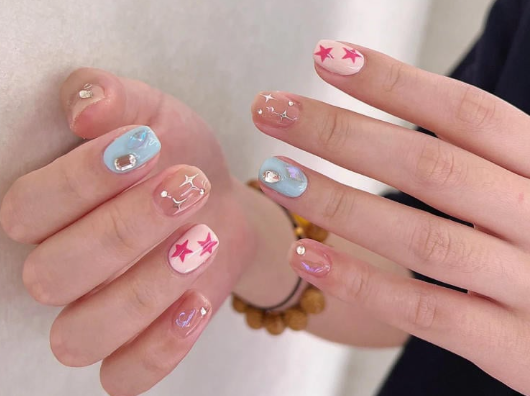 Tổng Hợp Mẫu Nail Màu Xanh Dương Nhạt Đẹp Nhẹ Nhàng Hot Nhất 2025 26 Bàn tay có móng tay được sơn màu pastel với họa tiết ngôi sao và trang trí kim loại.