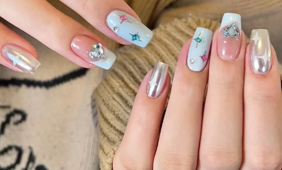 Tổng Hợp Mẫu Nail Màu Xanh Dương Nhạt Đẹp Nhẹ Nhàng Hot Nhất 2025 27 Bàn tay với móng tay sơn màu xanh nhạt, trang trí đá lấp lánh và họa tiết ngôi sao, tạo kiểu thời trang nổi bật.