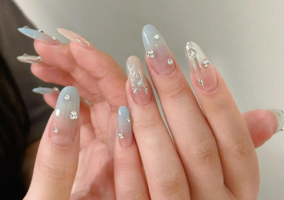 Tổng Hợp Mẫu Nail Màu Xanh Dương Nhạt Đẹp Nhẹ Nhàng Hot Nhất 2025 36 Bàn tay với móng tay được trang trí nghệ thuật, màu xanh nhạt và gắn đá lấp lánh.