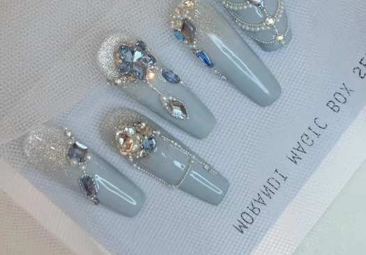 Tổng Hợp Mẫu Nail Màu Xanh Dương Nhạt Đẹp Nhẹ Nhàng Hot Nhất 2025 37 Bộ móng giả màu xám trang trí đá lấp lánh và họa tiết hoa văn tinh xảo trên nền giấy trắng.