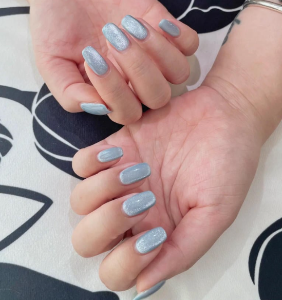 Tổng Hợp Mẫu Nail Màu Xanh Dương Nhạt Đẹp Nhẹ Nhàng Hot Nhất 2025 38 Hai bàn tay với móng tay được sơn màu xanh bạc lấp lánh, đặt trên nền vải hoa văn trắng đen.