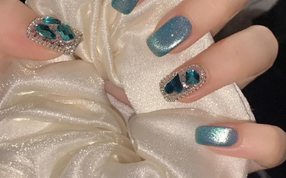 Tổng Hợp Mẫu Nail Màu Xanh Dương Nhạt Đẹp Nhẹ Nhàng Hot Nhất 2025 40 Bàn tay với móng tay được trang trí đá màu xanh lấp lánh, cầm một mảnh vải trắng bóng.