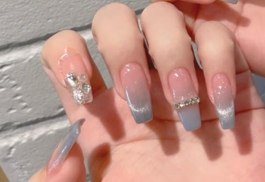 Tổng Hợp Mẫu Nail Màu Xanh Dương Nhạt Đẹp Nhẹ Nhàng Hot Nhất 2025 41 Bàn tay với móng tay dài, được sơn màu xanh nhạt, trang trí đá lấp lánh và hoa văn kim loại.