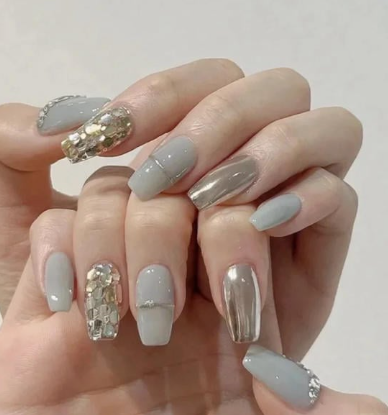 Tổng Hợp Mẫu Nail Màu Xanh Dương Nhạt Đẹp Nhẹ Nhàng Hot Nhất 2025 42 Bàn tay với móng tay được sơn màu xám và bạc, trang trí đá lấp lánh.