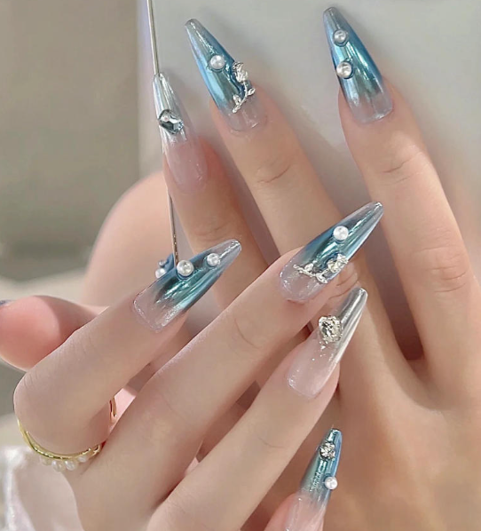 Tổng Hợp Mẫu Nail Màu Xanh Dương Nhạt Đẹp Nhẹ Nhàng Hot Nhất 2025 44 Bàn tay với móng tay dài, trang trí kiểu ombre xanh và bạc, đính hạt ngọc trai và phụ kiện kim loại nhỏ.