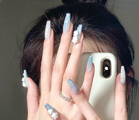Tổng Hợp Mẫu Nail Màu Xanh Dương Nhạt Đẹp Nhẹ Nhàng Hot Nhất 2025 48 Người cầm điện thoại, móng tay dài màu xanh ánh kim và đính phụ kiện hoa trắng.