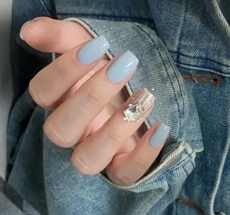 Tổng Hợp Mẫu Nail Màu Xanh Dương Nhạt Đẹp Nhẹ Nhàng Hot Nhất 2025 52 Người cầm tay áo khoác denim, móng tay sơn màu xanh nhạt, một móng được trang trí với đá lấp lánh.
