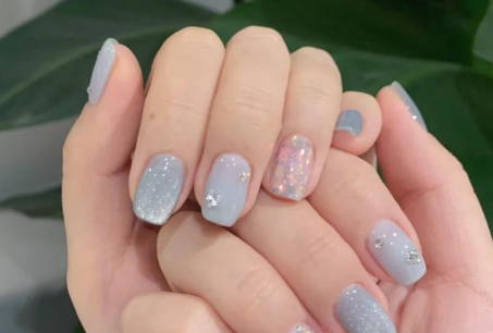Tổng Hợp Mẫu Nail Màu Xanh Dương Nhạt Đẹp Nhẹ Nhàng Hot Nhất 2025 53 Hai bàn tay với móng tay được sơn màu xanh nhạt và trang trí kim tuyến, một móng có họa tiết lấp lánh.