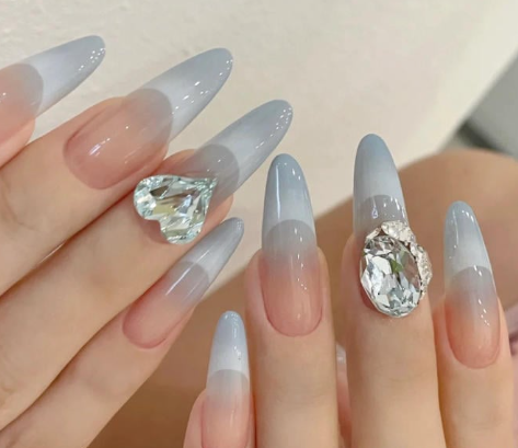 Tổng Hợp Mẫu Nail Màu Xanh Dương Nhạt Đẹp Nhẹ Nhàng Hot Nhất 2025 54 Bàn tay với móng tay dài, sơn màu ombre xanh nhạt, trang trí đá hình trái tim và viên lớn.