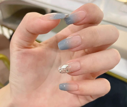Tổng Hợp Mẫu Nail Màu Xanh Dương Nhạt Đẹp Nhẹ Nhàng Hot Nhất 2025 56 Bàn tay với móng tay sơn màu xanh nhạt, móng đính đá và hoa văn trang trí tinh tế.