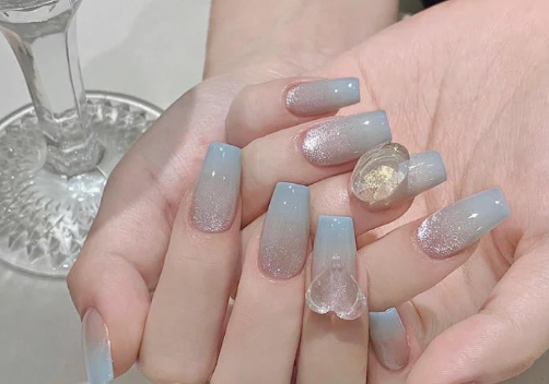 Tổng Hợp Mẫu Nail Màu Xanh Dương Nhạt Đẹp Nhẹ Nhàng Hot Nhất 2025 57 Bàn tay với móng tay dài, sơn màu xanh nhạt và trang trí lấp lánh, bên cạnh một ly thủy tinh.