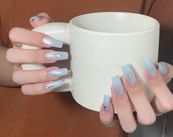 Tổng Hợp Mẫu Nail Màu Xanh Dương Nhạt Đẹp Nhẹ Nhàng Hot Nhất 2025 58 Bàn tay với móng tay sơn xanh nhạt và kim tuyến, cầm một chiếc cốc trắng.