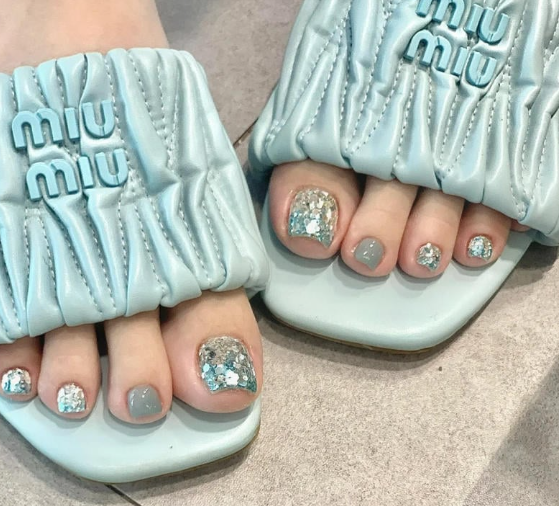 Tổng Hợp Mẫu Nail Màu Xanh Dương Nhạt Đẹp Nhẹ Nhàng Hot Nhất 2025 64 Bàn chân mang dép màu xanh nhạt với móng chân sơn màu xanh và trang trí kim tuyến lấp lánh.