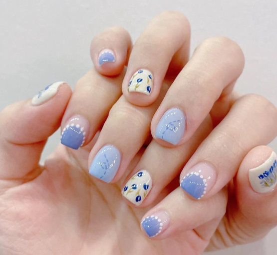 Tổng Hợp Mẫu Nail Màu Xanh Dương Nhạt Đẹp Nhẹ Nhàng Hot Nhất 2025 73 Bàn tay với móng tay được sơn màu xanh và trắng, trang trí họa tiết hoa văn tinh tế.
