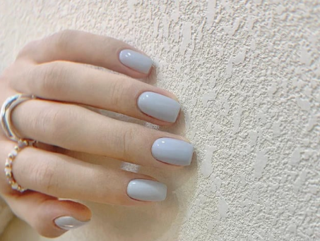 Tổng Hợp Mẫu Nail Màu Xanh Dương Nhạt Đẹp Nhẹ Nhàng Hot Nhất 2025 75 Bàn tay với móng sơn màu xám nhạt, đeo nhẫn, đặt trên bề mặt tường có kết cấu sần.
