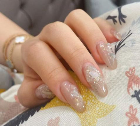 99+ mẫu nail đính đá vừa XINH vừa SANG cho nàng tự tin ra ngoài 11 Bàn tay với móng tay dài, sơn màu be, trang trí họa tiết trắng và lấp lánh, đặt trên vải có hoa văn.