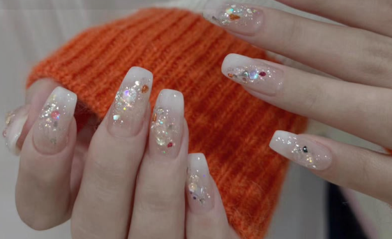 99+ mẫu nail đính đá vừa XINH vừa SANG cho nàng tự tin ra ngoài 12 Tay với móng tay dài, sơn màu nhạt và trang trí lấp lánh, đặt trên nền áo len màu cam.