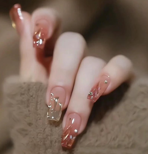 99+ mẫu nail đính đá vừa XINH vừa SANG cho nàng tự tin ra ngoài 20 Bàn tay với móng tay dài được trang trí hoa văn kim loại sáng bóng, nền màu nâu ấm áp.