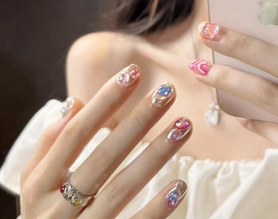 99+ mẫu nail đính đá vừa XINH vừa SANG cho nàng tự tin ra ngoài 26 Người cầm điện thoại, móng tay được sơn màu sắc rực rỡ, đeo nhẫn và mặc áo trễ vai trắng.