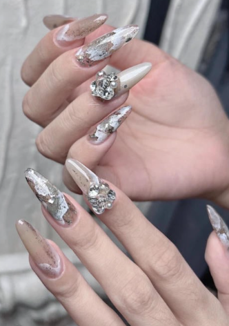 99+ mẫu nail đính đá vừa XINH vừa SANG cho nàng tự tin ra ngoài 35 Đôi tay với móng dài, trang trí họa tiết và đính đá, nền màu nâu và trắng, tạo kiểu nghệ thuật tinh tế.