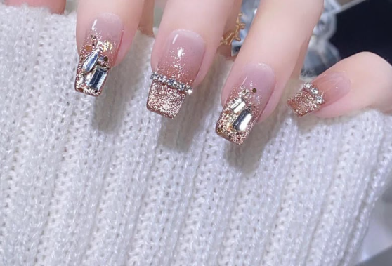 99+ mẫu nail đính đá vừa XINH vừa SANG cho nàng tự tin ra ngoài 38 Bàn tay với móng tay đính kim tuyến và đá lấp lánh, trên nền áo len màu trắng.