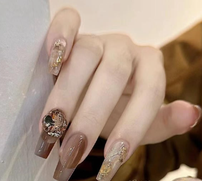 99+ mẫu nail đính đá vừa XINH vừa SANG cho nàng tự tin ra ngoài 39 Tay với móng được sơn màu nâu và trang trí bằng họa tiết lấp lánh, đặt trên nền màu trắng.
