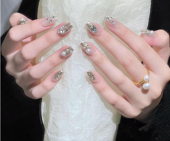 99+ mẫu nail đính đá vừa XINH vừa SANG cho nàng tự tin ra ngoài 45 Hai bàn tay với móng tay được trang trí lấp lánh và đính đá, một tay đeo nhẫn ngọc trai.