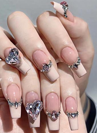 99+ mẫu nail đính đá vừa XINH vừa SANG cho nàng tự tin ra ngoài 46 Bàn tay với móng tay dài màu nude, trang trí đá quý hình trái tim và họa tiết lấp lánh.