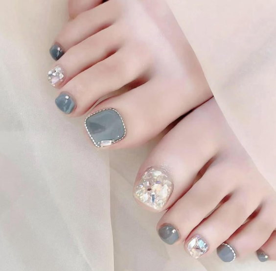 99+ mẫu nail đính đá vừa XINH vừa SANG cho nàng tự tin ra ngoài 60 Bàn chân với móng được sơn màu xám và trang trí đá lấp lánh, đặt trên nền vải trắng mịn.