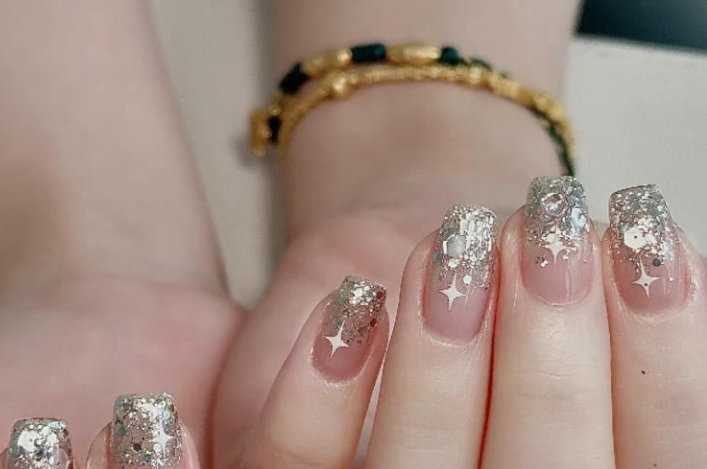 100+ Mẫu Nail Nhũ Đẹp Lấp Lánh Giúp Phái Nữ Tỏa Sáng Thời Thượng 3 Bàn tay có móng tay được trang trí với lớp sơn lấp lánh, đính đá và họa tiết ngôi sao, đeo vòng tay màu vàng.