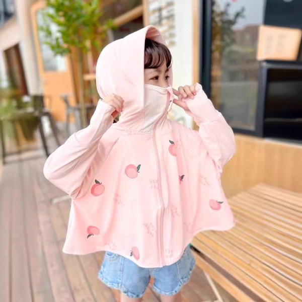 Trẻ em mặc áo hồng có mũ, họa tiết trái đào, đứng trên sàn gỗ cạnh ghế gỗ và cửa kính.