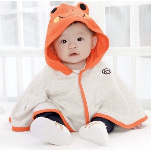 Em bé mặc áo choàng xám có mũ cam, ngồi trong phòng sáng.