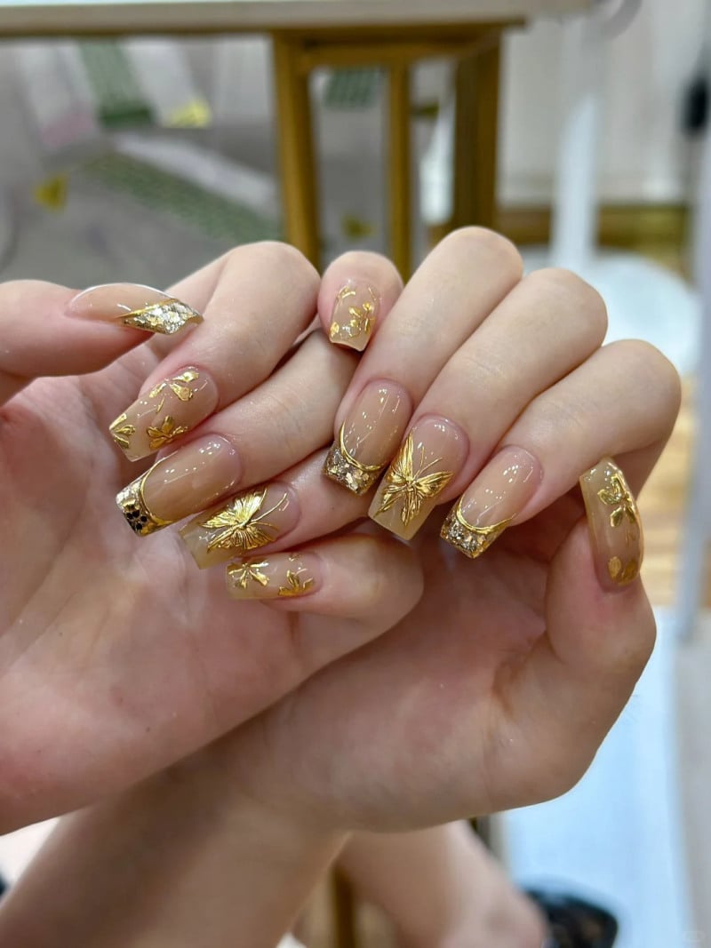 Bàn tay với móng tay được trang trí hoa văn và họa tiết màu vàng lấp lánh, nền trong suốt.