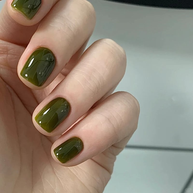 Bàn tay với móng tay sơn màu xanh lục, nền màu xám trắng.