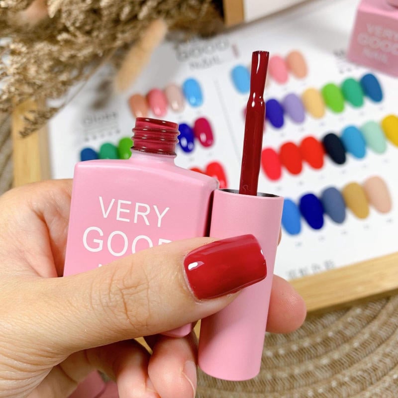 bang-mau-very-good-nail__11__91f54811752544e9b033748d617491d0 Tay cầm lọ sơn móng tay màu hồng, nắp mở, nền có bảng màu sơn móng tay đa dạng.